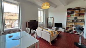 Um quarto com uma mesa de jantar, um sofá, uma televisão, uma estante de livros e uma janela com vista.