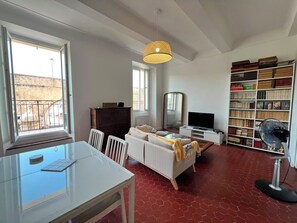 Ein Zimmer mit Esstisch, einer Couch, einem Fernseher, einem Bücherregal und einem Fenster mit Blick.