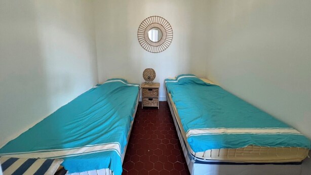 Quarto com duas camas de solteiro, uma mesinha de cabeceira com luminária e espelho fixado na parede.