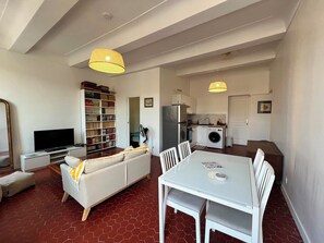 A compact living space with a sofa, a dining table, a bookshelf, a television, and a kitchen area with a refrigerator and washing machine. - Newly renovated apart in the heart of Old Antibes (Antibes)