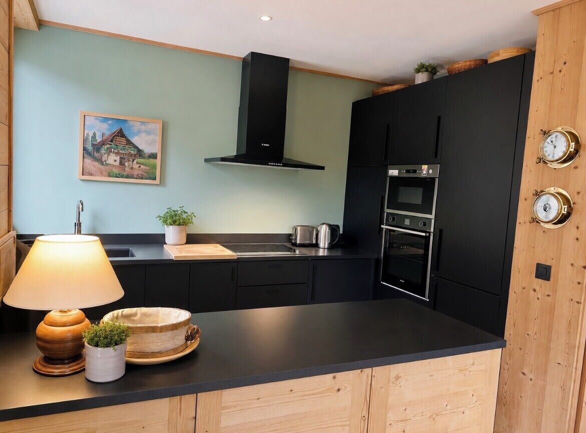 A modern kitchen with black cabinets, a stove, and a microwave. There is a painting on the wall and a lamp on the counter.