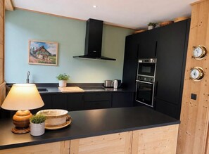 A modern kitchen with black cabinets, a stove, and a microwave. There is a painting on the wall and a lamp on the counter. - Spacious and bright with balcony & Mont Blanc view (Chamonix-Mont-Blanc)