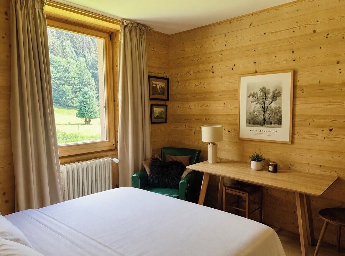 Una habitación con cama, escritorio, silla, lámpara y ventana con cortinas.