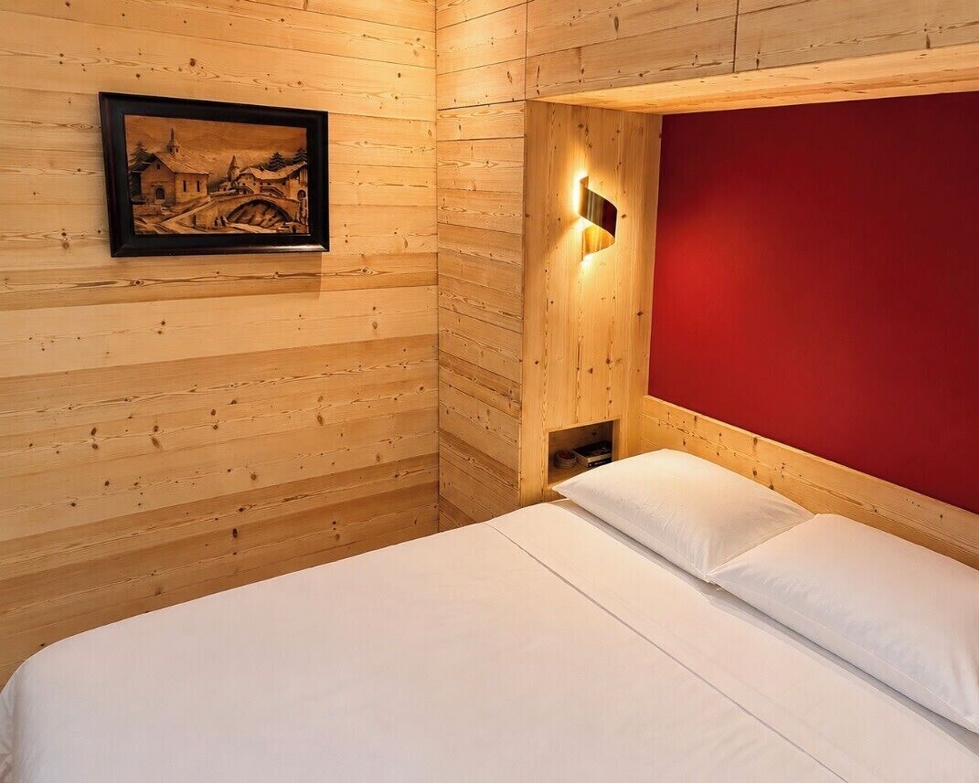 A wooden room with a bed, a wall-mounted light, and a framed picture.