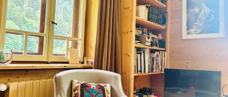 Una habitación acogedora con una estantería de madera, un sillón cómodo y un televisor.