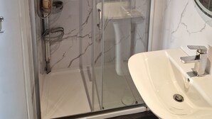Une salle de bain avec une douche à parois de verre, un lavabo blanc et des murs en marbre.