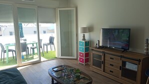 Ein Wohnzimmer mit Fernseher, Couchtisch, Schrank und einer Schiebetür zu einem Außenbereich mit Stühlen und einem Tisch.