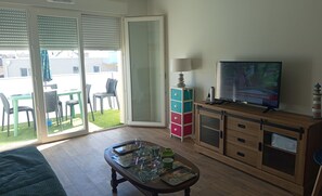 Ein Wohnzimmer mit Fernseher, Couchtisch, Schrank und einer Schiebetür zu einem Außenbereich mit Stühlen und einem Tisch.