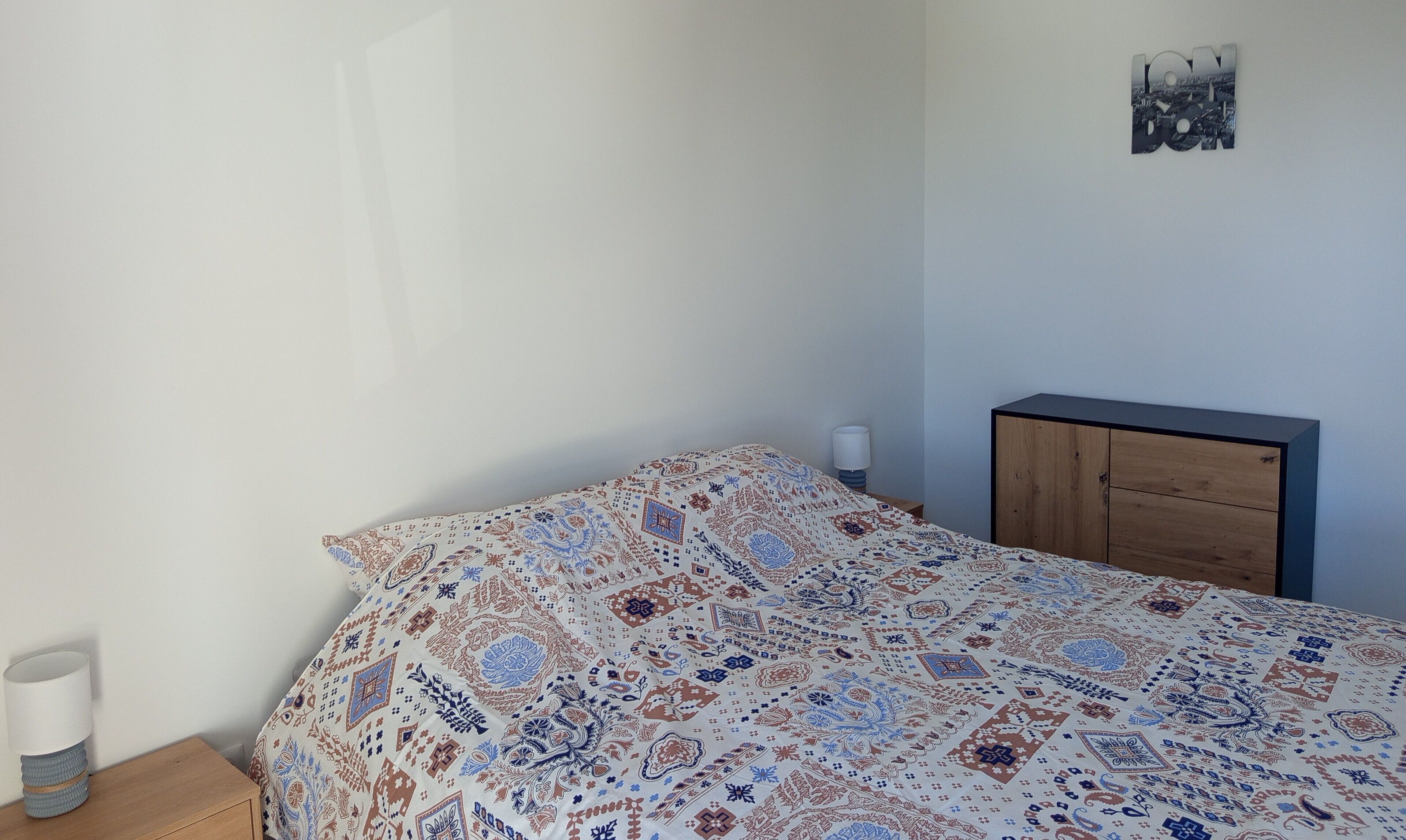 A bedroom with a bed, a nightstand, a lamp, a wooden cabinet, and a wall decoration.