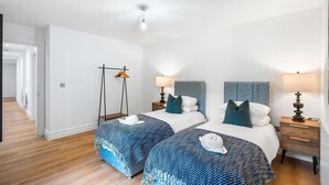 A hotel room with two beds, a wardrobe, bedside lamps, a hanging coat rack, and a ceiling light. - Urban Breeze By My Getaways (Brighton)
