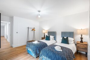 Ein Hotelzimmer mit zwei Betten, einem Kleiderschrank, Nachttischlampen, einem Kleiderhaken und einer Deckenleuchte.