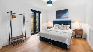 A bedroom with a bed, bedside tables, a hanging rack, and a view through a glass door. - Urban Breeze By My Getaways (Brighton)