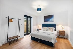 Ein Schlafzimmer mit Bett, Nachttischen, einer Garderobe und Blick durch eine Glastür.