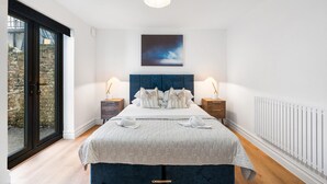 A bedroom with a large bed, a view through a sliding door, a blue headboard, and a ceiling light. - Urban Breeze By My Getaways (Brighton)