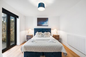Ein Schlafzimmer mit einem großen Bett, Blick durch eine Schiebetür, einem blauen Kopfteil und einer Deckenleuchte.