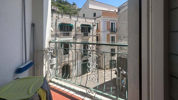 A balcony with a metal railing, a green mat, and a view of buildings with multiple windows and balconies. - Apartament in Minori (Minori)