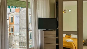 A hotel room with a television on a wooden stand, a bed with a yellow bedspread, and a view of the outside balcony. - Apartament in Minori (Minori)