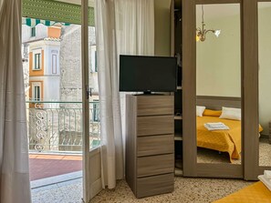 A hotel room with a television on a wooden stand, a bed with a yellow bedspread, and a view of the outside balcony. - Apartament in Minori (Minori)