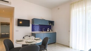A modern kitchen with blue cabinets, a dining table with chairs, and a flat-screen TV mounted on the wall. - Donna Maria - Marialuce (Amalfi)