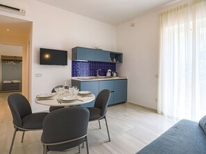 Eine moderne Küche mit blauen Schränken, einem Esstisch mit Stühlen und einem an der Wand befestigten Flachbildfernseher.