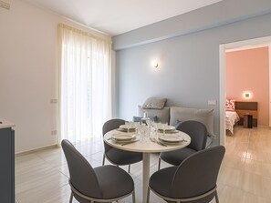 Ein Essbereich mit einem runden Tisch, gedeckt für vier Personen, einer Couch und einem Bett im Hintergrund.