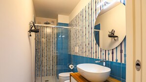 A modern bathroom with a glass shower enclosure, a white sink with a wooden countertop, and a blue and white tiled wall. - Donna Maria - Marialuce (Amalfi)