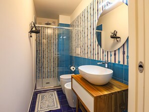 Ein modernes Badezimmer mit Duschkabine aus Glas, einem weißen Waschbecken mit Holzablage und einer Wand mit blauen und weißen Fliesen.