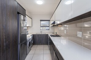 A modern kitchen with a built-in washing machine, a gas stove, and a window providing natural light. - Modern 3-bed Garden Pool Gym by Ctha (Cape Town)