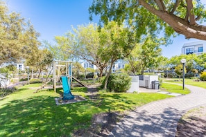 A park with a playground, a paved walkway, and a building in the background. - Modern 3-bed Garden Pool Gym by Ctha (Cape Town)