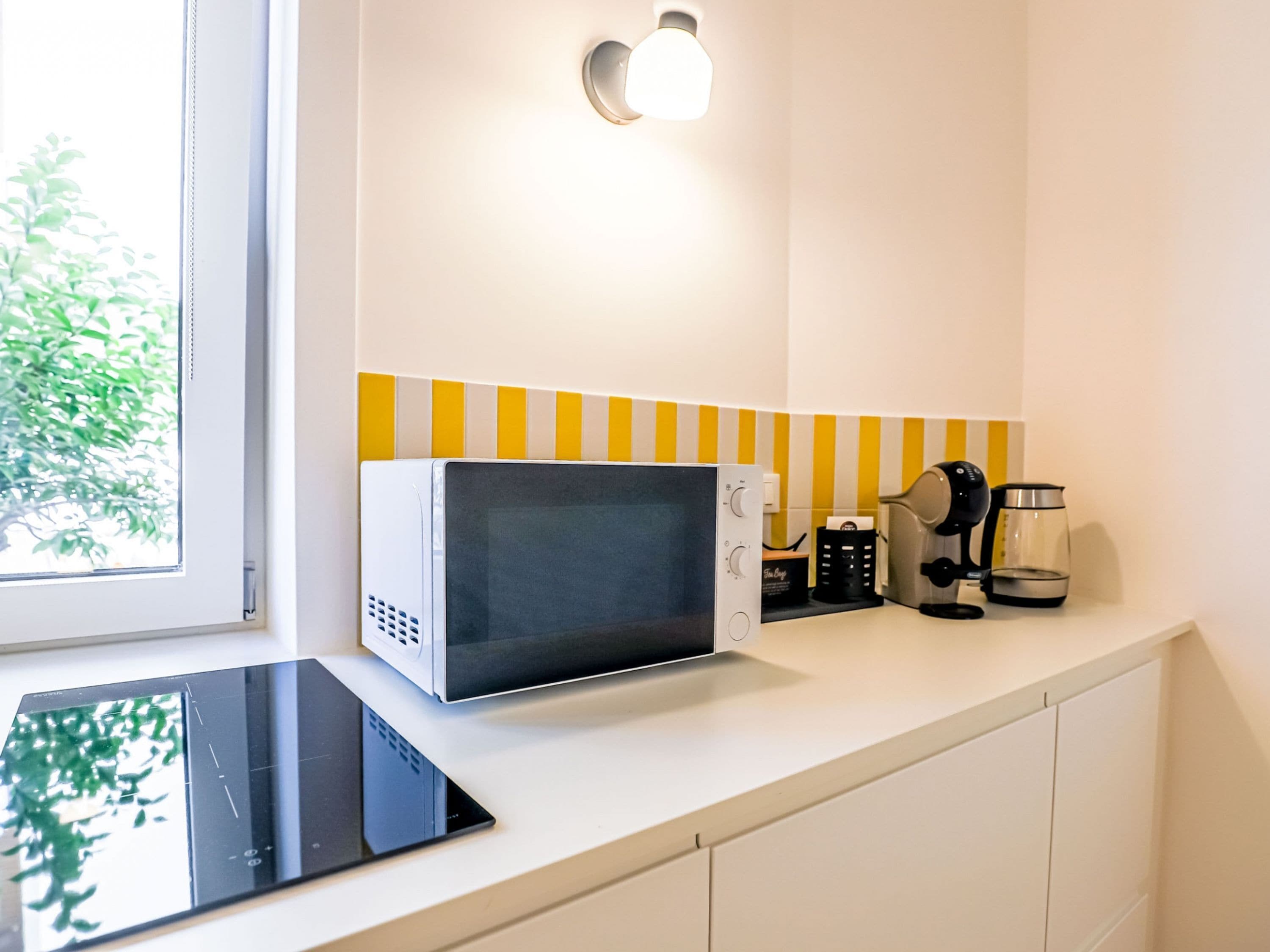 A kitchen with a microwave, coffee maker, and a kettle on the counter.