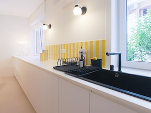 A modern kitchen with a black sink, white cabinets, and a yellow-striped backsplash. - Blue Elina - Amami Viaggi Collection (Salerno)