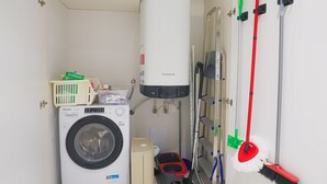 A compact laundry room with a front-loading washing machine, a tall water heater, a vacuum cleaner, and a mop rack. - Blue Elina - Amami Viaggi Collection (Salerno)