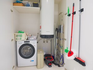 A compact laundry room with a front-loading washing machine, a tall water heater, a vacuum cleaner, and a mop rack. - Blue Elina - Amami Viaggi Collection (Salerno)