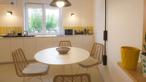 A modern kitchen with a round dining table, wicker chairs, and a black pendant light. - Blue Elina - Amami Viaggi Collection (Salerno)