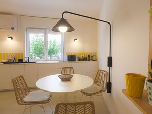 A modern kitchen with a round dining table, wicker chairs, and a black pendant light. - Blue Elina - Amami Viaggi Collection (Salerno)