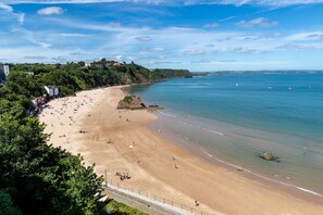 A beach with a rocky outcrop, a sandy shore, and a clear blue sky. - Royal Victoria Court 7 - Tenby Harbour Sea Views (Tenby)