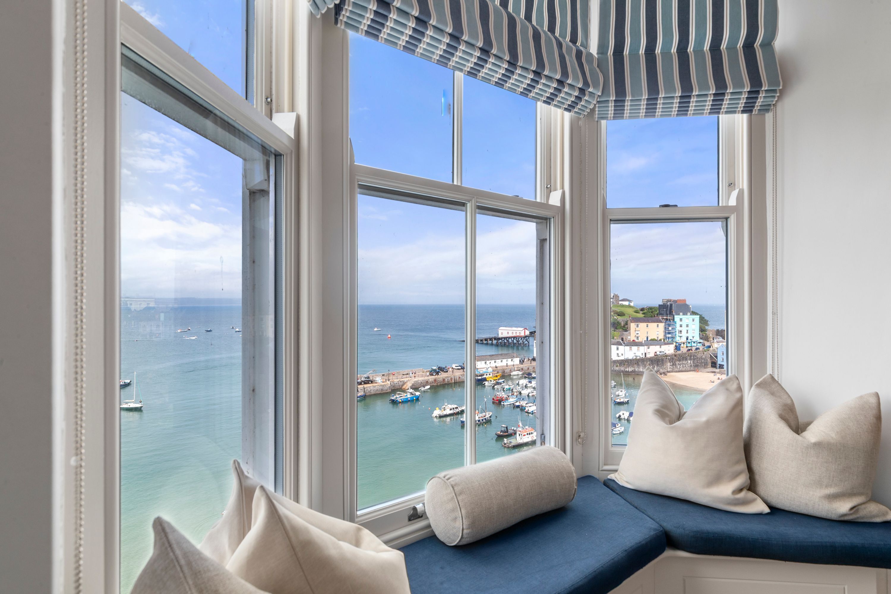 A room with a view of a harbor, a window seat with cushions, and a striped valance.
