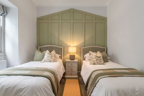 A bedroom with two beds, a nightstand with a lamp, and a window with curtains. - Royal Victoria Court 7 - Tenby Harbour Sea Views (Tenby)