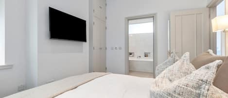 A bedroom with a bed, a television mounted on the wall, a wardrobe, and a bathroom visible through an open door.