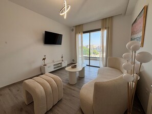 Ein modernes Wohnzimmer mit Flachbildfernseher, einer weißen Konsole, einem runden Couchtisch und zwei beigefarbenen Sofas.