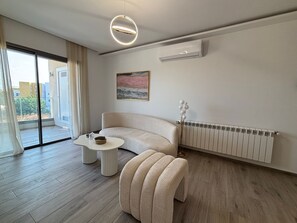 Ein modernes Wohnzimmer mit einer gebogenen Couch, einem runden Couchtisch, einem Bild an der Wand und einer Heizung.