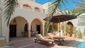 A courtyard with lounge chairs, a table, and a pool.