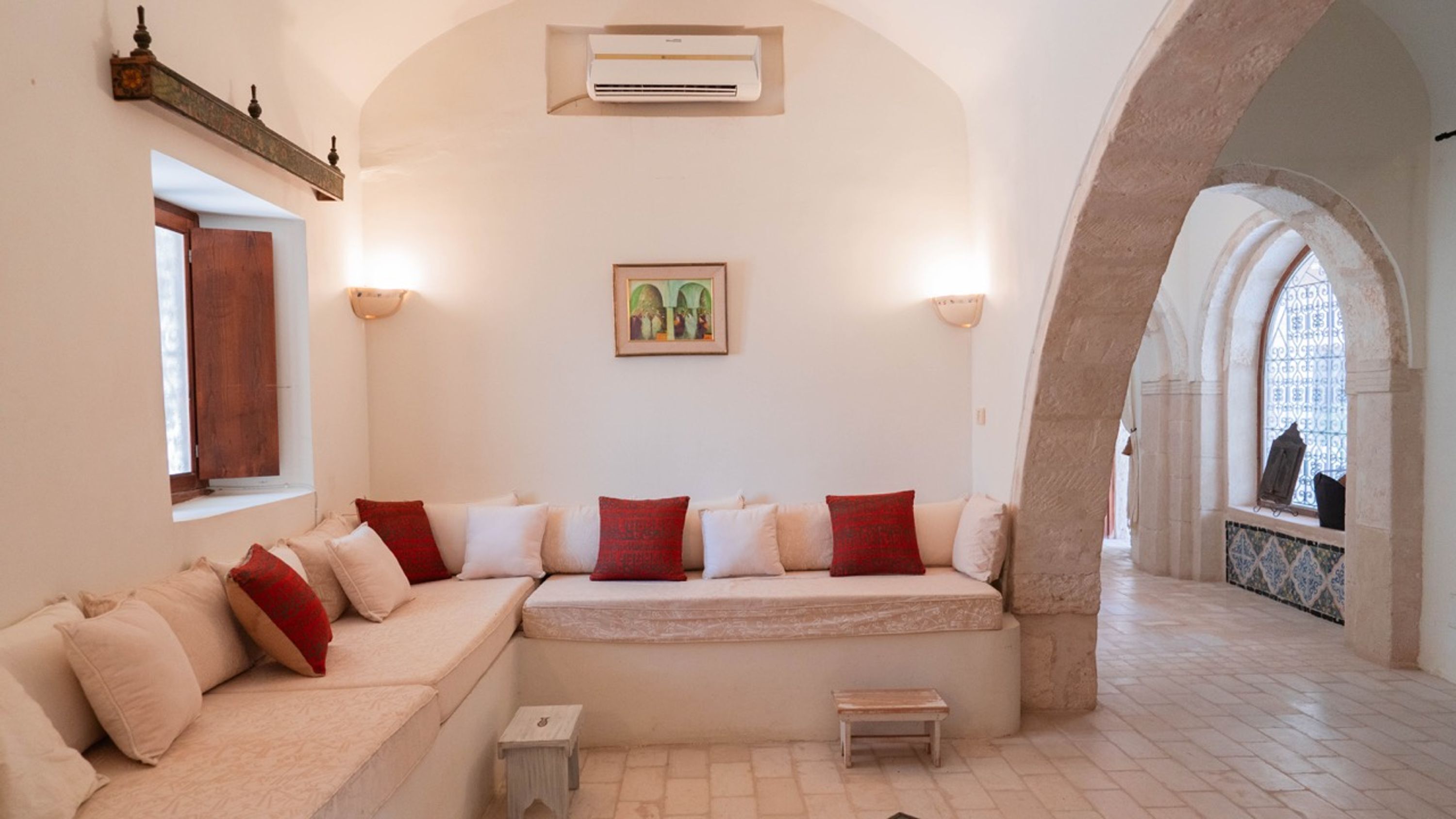 A room with a sofa, a small table, an air conditioning unit, a framed picture, and an arched doorway.