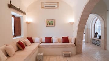 A room with a sofa, a small table, an air conditioning unit, a framed picture, and an arched doorway.