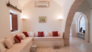 A room with a sofa, a small table, an air conditioning unit, a framed picture, and an arched doorway.