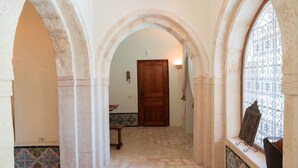 A corridor with stone flooring, a wooden door, and a window with decorative iron bars. - Dar Meryem Djerba Houch Avec Piscine (Erriadh)