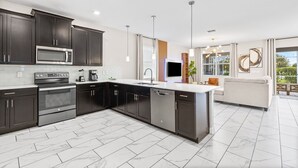 A modern kitchen with dark cabinetry, a built-in microwave, and a dishwasher. - Themed 9BR Villa Pool Game Room Champions Gate (Davenport)