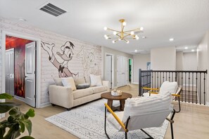 A modern living room with a large mural, a sofa, a coffee table, and a chair. - Themed 9BR Villa Pool Game Room Champions Gate (Davenport)