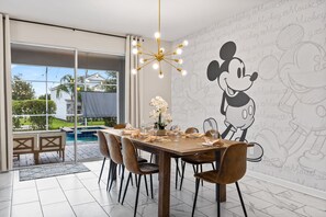 A dining area with a large Mickey Mouse mural, a pool, and a modern chandelier. - Themed 9BR Villa Pool Game Room Champions Gate (Davenport)