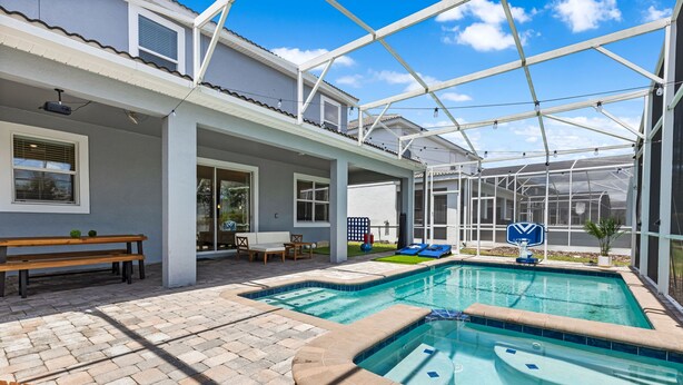 A covered outdoor swimming pool area with a patio, seating, and a greenhouse structure. - Themed 9BR Villa Pool Game Room Champions Gate (Davenport)